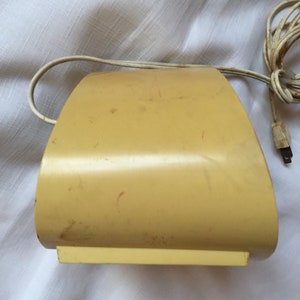 May include: A yellow vintage alarm clock with a cord. The clock is shaped like a half-circle and has a slightly worn surface.