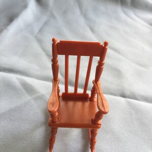 K&ouml;nnte beinhalten: Ein orangefarbener Miniatur-Schaukelstuhl mit schlichtem Design. Der Stuhl hat eine hohe R&uuml;ckenlehne und geschwungene Armlehnen. Die Schaukelbasis besteht aus gedrehtem Holz.
