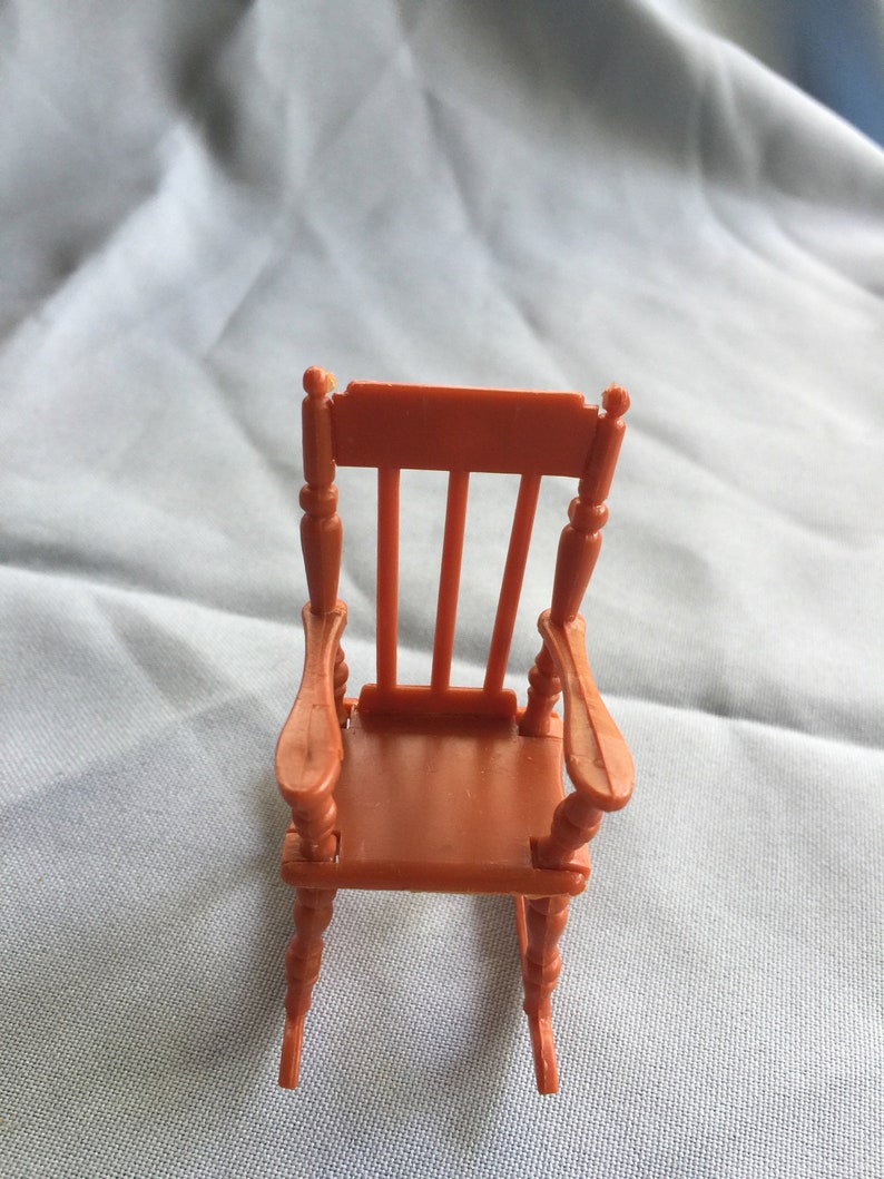 K&ouml;nnte beinhalten: Ein orangefarbener Miniatur-Schaukelstuhl mit schlichtem Design. Der Stuhl hat eine hohe R&uuml;ckenlehne und geschwungene Armlehnen. Die Schaukelbasis besteht aus gedrehtem Holz.