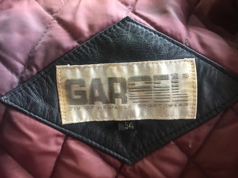 Pu&ograve; includere: Una toppa in pelle nera con un'etichetta bianca che recita "GARCEY DIV. OF RELIABLE SPORTSWEAR" e un'etichetta di taglia che indica "54".