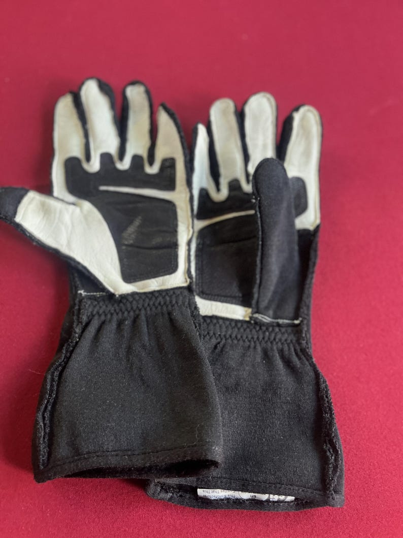 Puede incluir: Un par de guantes de carreras en blanco y negro. Los guantes tienen palmas y dedos de cuero blanco, con tela negra en el dorso de la mano y la mu&ntilde;eca. Dise&ntilde;ados para agarre y protecci&oacute;n.