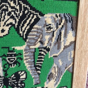 May include: A framed needlepoint tapestry with a green background and a variety of animals including a zebra, an elephant, and a turtle. The animals are stitched in various shades of gray, black, and white.