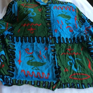 K&ouml;nnte beinhalten: Ein lang&auml;rmliges Hemd mit Kn&ouml;pfen und einem farbenfrohen abstrakten Muster in Blaut&ouml;nen, Gr&uuml;n, Rot und Schwarz. Das Muster zeigt geometrische Formen und Wellenlinien.