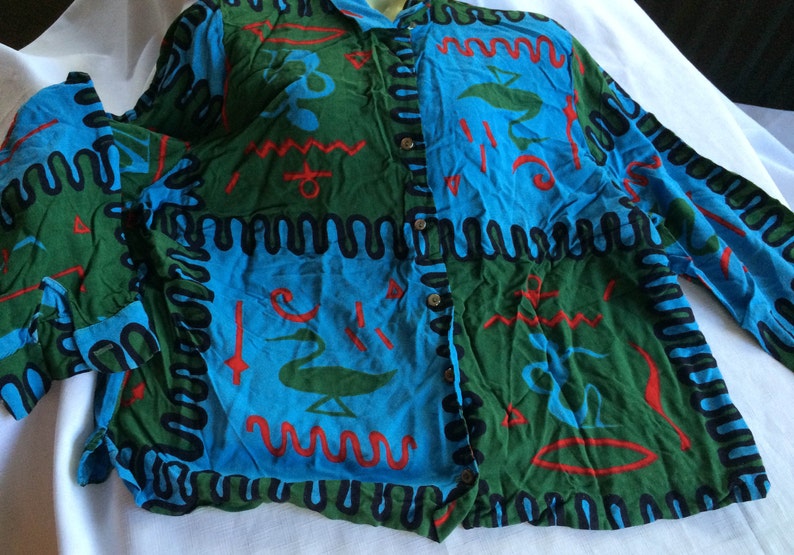 K&ouml;nnte beinhalten: Ein lang&auml;rmliges Hemd mit Kn&ouml;pfen und einem farbenfrohen abstrakten Muster in Blaut&ouml;nen, Gr&uuml;n, Rot und Schwarz. Das Muster zeigt geometrische Formen und Wellenlinien.