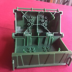 May include: A green plastic box with a hinged lid, open to reveal a compartment with multiple small holes. The box has a textured surface and a handle on the side.
