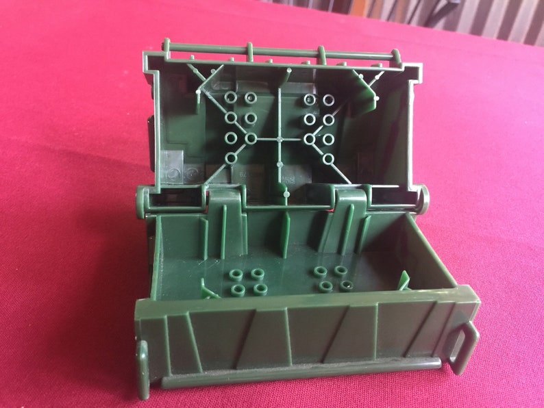 May include: A green plastic box with a hinged lid, open to reveal a compartment with multiple small holes. The box has a textured surface and a handle on the side.