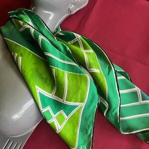 May include: A green and white silk scarf with a geometric pattern. The scarf is folded and draped over a mannequin's neck.
