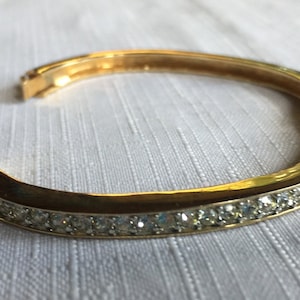 Peut inclure: Un bracelet jonc en or avec une rangée de strass clairs autour du bord.