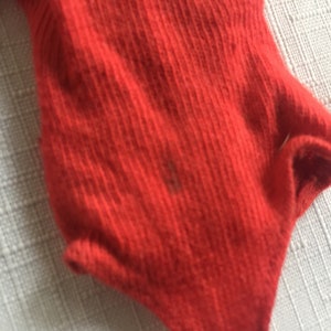 May include: Red ribbed fabric with a slight texture. The fabric is folded over on itself, creating a curved shape.