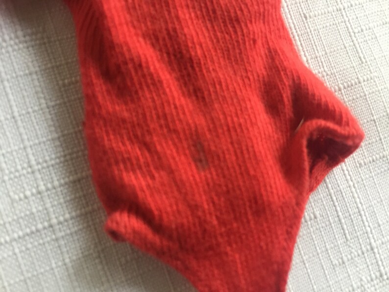May include: Red ribbed fabric with a slight texture. The fabric is folded over on itself, creating a curved shape.