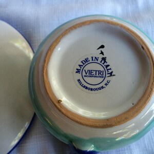 May include: A white ceramic bowl with a blue and green rim. The bowl has a sticker on the bottom that reads "Made in Italy, Vietri Incorporated, Hillsborough, N.C."