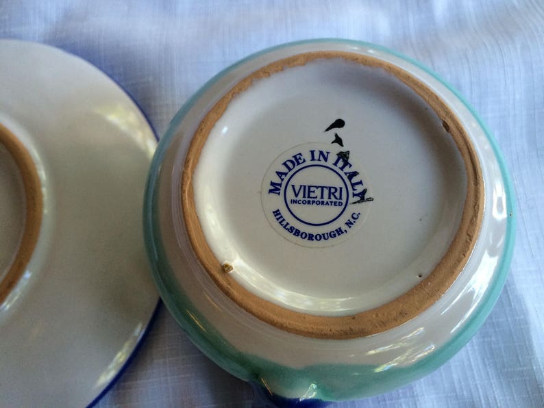 May include: A white ceramic bowl with a blue and green rim. The bowl has a sticker on the bottom that reads "Made in Italy, Vietri Incorporated, Hillsborough, N.C."