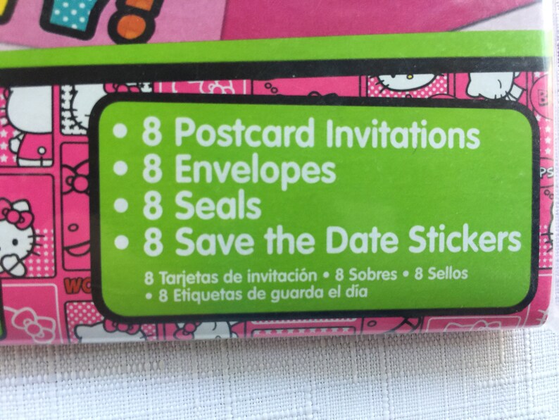 May include: Green and white label with a pink and white Hello Kitty pattern in the background. The label lists the contents of the party supplies: 8 Postcard Invitations, 8 Envelopes, 8 Seals, and 8 Save the Date Stickers. The label also includes the text in Spanish: 8 Tarjetas de invitaci&oacute;n 8 Sobres 8 Sellos 8 Etiquetas de guarda el d&iacute;a.
