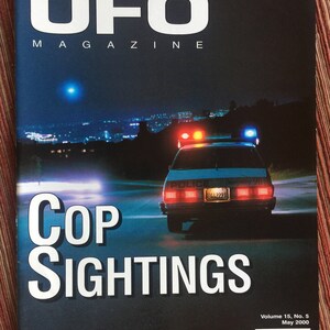Puede incluir: UFO Magazine, Volumen 15, N.&ordm; 5, mayo de 2000, lleva el t&iacute;tulo Cop Sightings. La portada muestra una escena nocturna de un coche de polic&iacute;a con luces de emergencia rojas y azules activadas en una carretera oscura y una luz azul brillante.