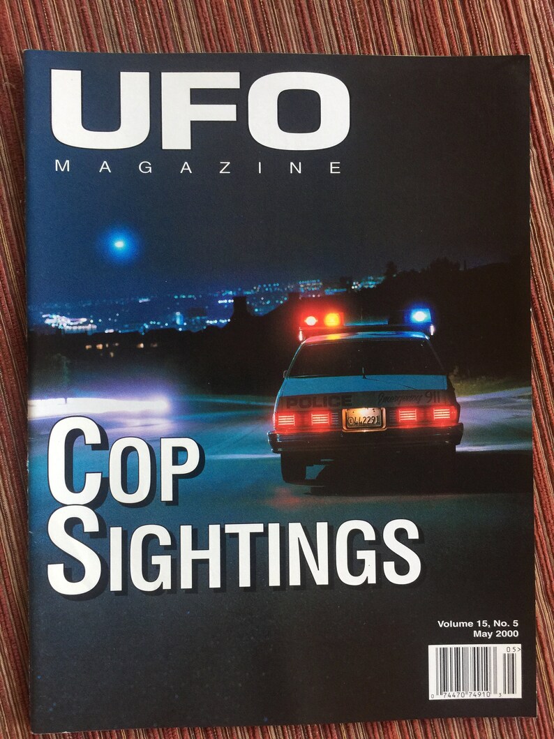 Puede incluir: UFO Magazine, Volumen 15, N.&ordm; 5, mayo de 2000, lleva el t&iacute;tulo Cop Sightings. La portada muestra una escena nocturna de un coche de polic&iacute;a con luces de emergencia rojas y azules activadas en una carretera oscura y una luz azul brillante.
