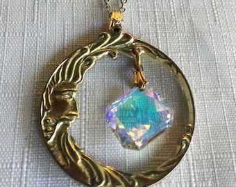 Puede incluir: Un collar dorado con un colgante de media luna con una cara y un cristal iridiscente colgante.