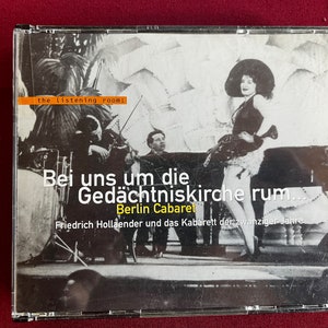 Puede incluir: Una fotografía en blanco y negro de una actuación de cabaret en Berlín, Alemania. La foto muestra a una mujer con un traje de plumas y un sombrero, cantando y bailando en el escenario. El texto en la portada del CD dice "Bei uns um die Gedächtniskirche rum... Berlin Cabaret Friedrich Hollaender und das Kabarett der zwanziger Jahre."