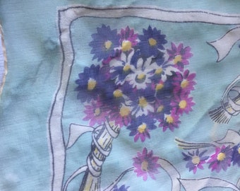 Op de afbeelding: Een lichtblauw zakdoek met een witte rand en een bloemenpatroon van paarse, roze en gele bloemen. De bloemen zijn gerangschikt in een boeket met een wit lint.