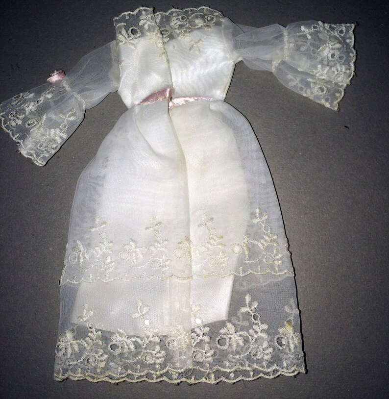 Puede incluir: Un vestido blanco de gasa con detalles de encaje y una cinta de raso rosa alrededor de la cintura.