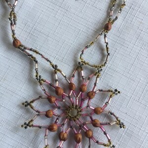 Pode incluir: Um colar de contas com um pingente em forma de estrela feito de contas marrons e prateadas. O pingente &eacute; rodeado por contas cor-de-rosa e douradas.