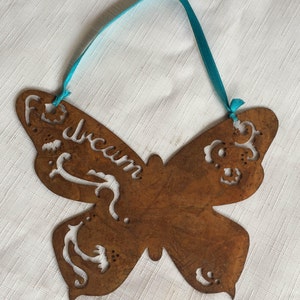 May include: A rusty metal butterfly ornament with a turquoise ribbon for hanging. The butterfly has cut-out designs and the word "Dream" is written on one wing.