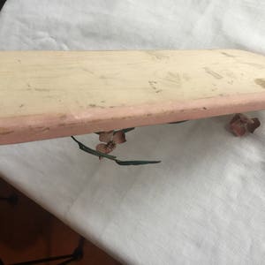 May include: A light pink wooden tray with a slightly rounded edge. The tray is decorated with a floral design in shades of pink and green.