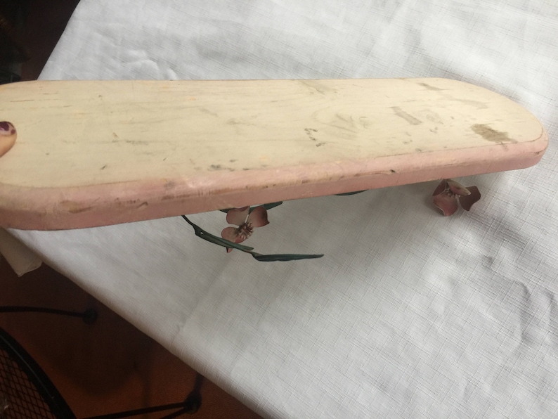 May include: A light pink wooden tray with a slightly rounded edge. The tray is decorated with a floral design in shades of pink and green.