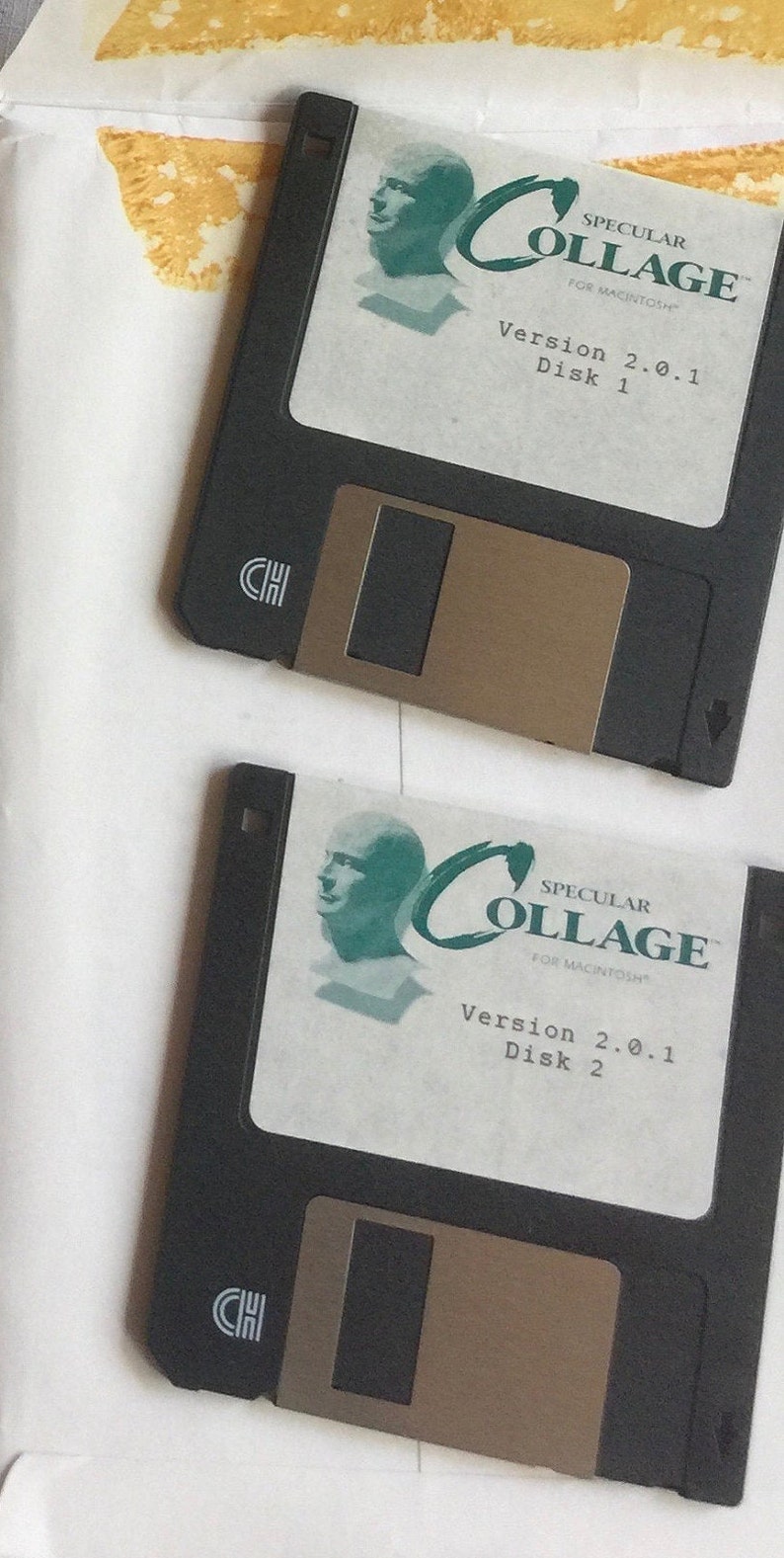 Puede incluir: Dos disquetes negros de 3,5 pulgadas etiquetados "Specular Collage for Macintosh" con un logotipo verde y blanco. El disquete superior est&aacute; etiquetado "Disk 1" y el disquete inferior est&aacute; etiquetado "Disk 2". Ambos disquetes est&aacute;n etiquetados "Version 2.0.1".