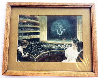 May include: A framed painting depicting a scene from a theater. Two women are seated in a box, watching a performance on stage. The stage is lit with spotlights, and the performers are dressed in white costumes. The audience is seated in the orchestra and balcony levels.