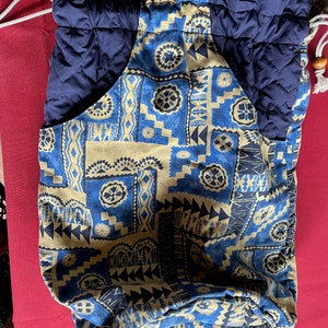 May include: A blue and beige drawstring bag with a quilted navy blue lining. The bag features a geometric pattern with a Polynesian-inspired design.