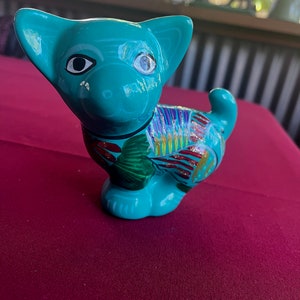 May include: A teal blue ceramic figurine of a dog with colorful painted details. The dog has black eyes and a white nose.