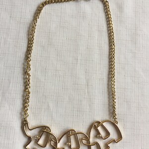 May include: A gold chain necklace with a pendant of three connected elephant silhouettes. Each elephant has a single rhinestone in the center.
