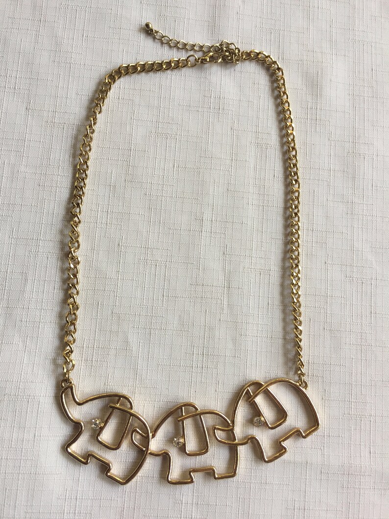 May include: A gold chain necklace with a pendant of three connected elephant silhouettes. Each elephant has a single rhinestone in the center.