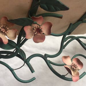 May include: A metal wall decor piece featuring a stylized floral design with pink flowers and green leaves.