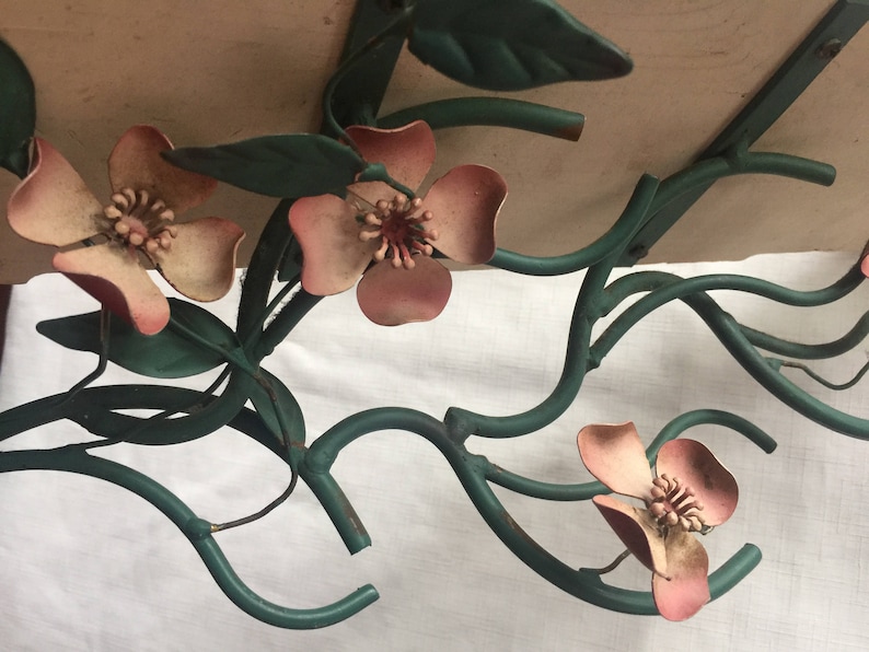 May include: A metal wall decor piece featuring a stylized floral design with pink flowers and green leaves.