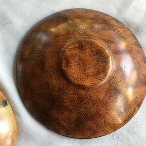 May include: A wooden bowl with a brown and orange finish. The bowl has a textured surface and a slightly raised center.