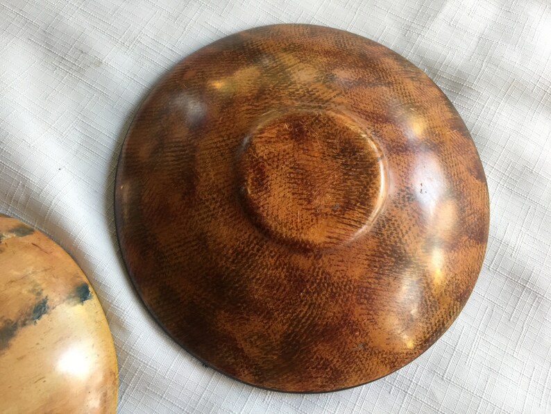 May include: A wooden bowl with a brown and orange finish. The bowl has a textured surface and a slightly raised center.