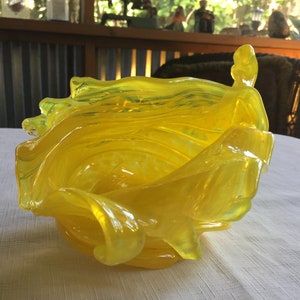 May include: A yellow glass bowl with a wavy, organic design. The bowl is made of clear glass with a yellow tint.