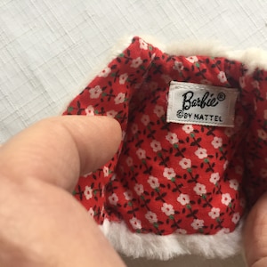 May include: A white faux fur jacket with a red and white floral lining. The jacket has a label that reads "Barbie&reg; &copy; by Mattel."