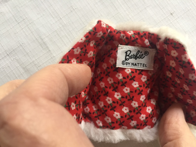 May include: A white faux fur jacket with a red and white floral lining. The jacket has a label that reads "Barbie&reg; &copy; by Mattel."