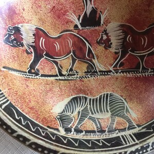 May include: A round, red and black, hand-painted, ceramic plate with a black and white zebra, two lions, and a tree design.