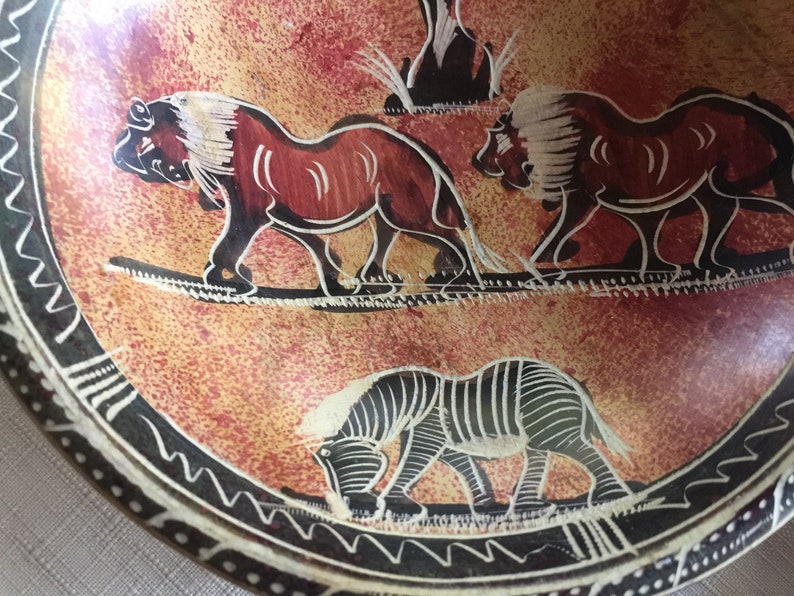 May include: A round, red and black, hand-painted, ceramic plate with a black and white zebra, two lions, and a tree design.