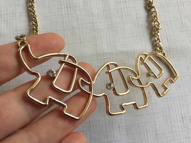 May include: Gold necklace with three linked elephant pendants, each with a clear rhinestone in the center.
