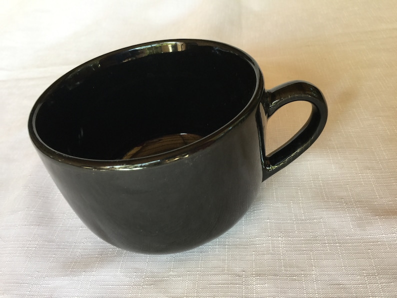May include: A large, black ceramic mug with a rounded shape and a handle. The mug is empty and sitting on a white surface.