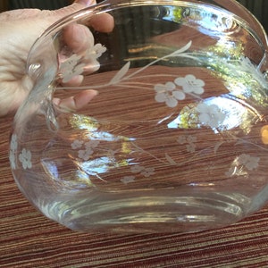 May include: A clear glass bowl with a floral design etched into the glass. The bowl has a rounded shape and a wide rim.