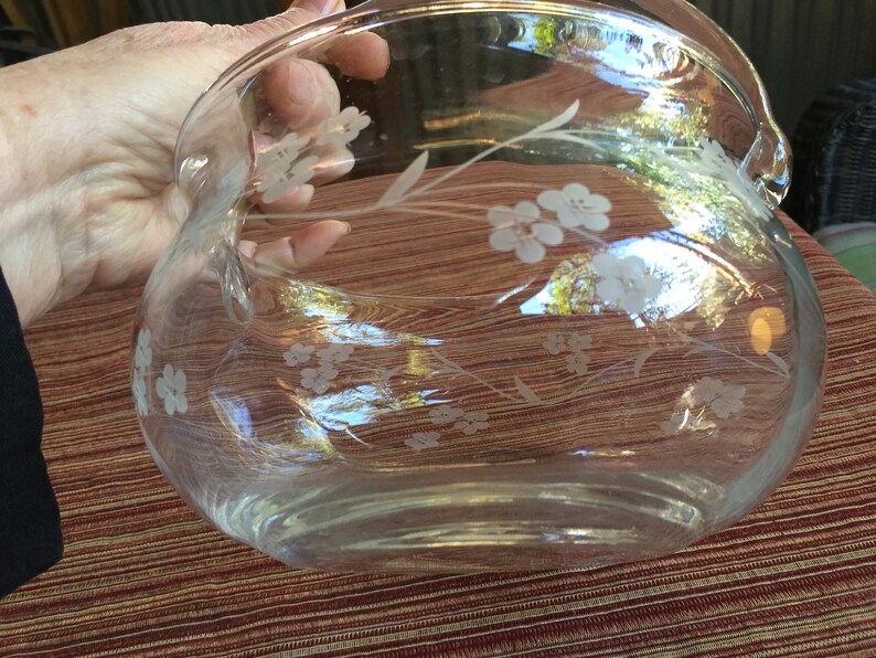 May include: A clear glass bowl with a floral design etched into the glass. The bowl has a rounded shape and a wide rim.