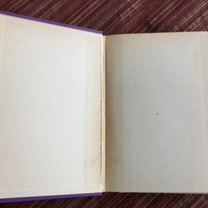 May include: An open book with blank pages and a purple cover. The book is lying flat on a red surface.