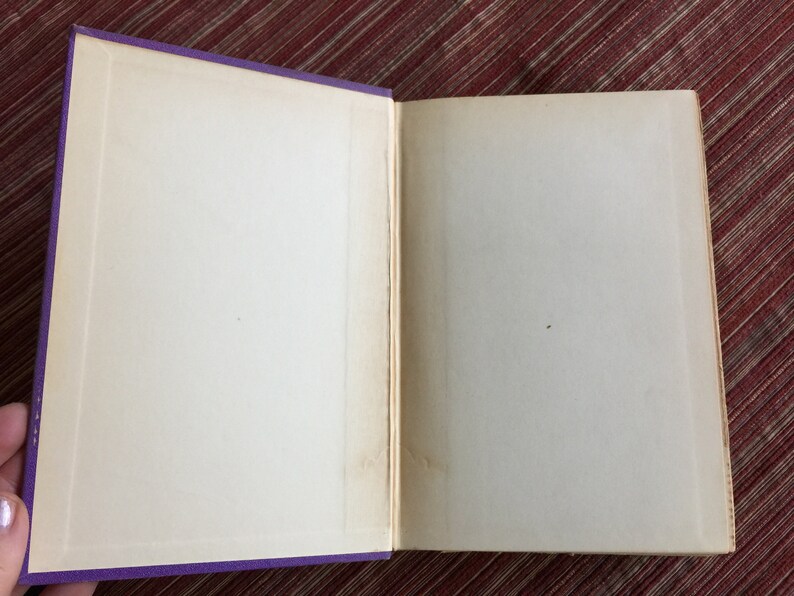 May include: An open book with blank pages and a purple cover. The book is lying flat on a red surface.