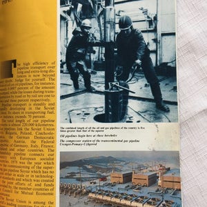 May include: A black and white photo of two workers operating a large metal pipe. The photo is taken from a low angle, showing the workers in action. The text below the photo reads: "The combined length of all the oil and gas pipelines of the country is five times greater than that of the equator. Oil pipelines begin here at these boreholes. The compressor station of the transcontinental gas pipeline Urengoi-Pomary-Uzhgorod."