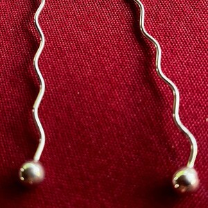 May include: A pair of silver earrings with a wavy design and a small ball at the end of each earring.